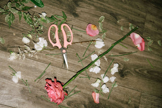 Pink scissors on a wooden surface with flowers and greenery at Plum Social floral studio in Denver, CO.