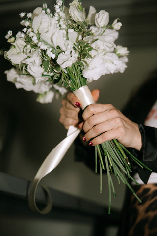 A florist at Plum Social floral studio in Denver, Colorado holding a bouquet of white flowers with a blurred background