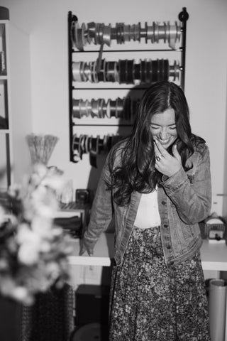 Woman laughing in a room with shelves and plants at Plum Social floral studio in Denver, CO.
